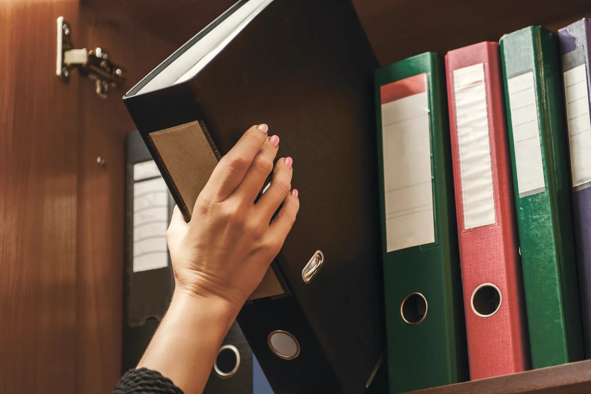 A hand taking a binder from an office shelf