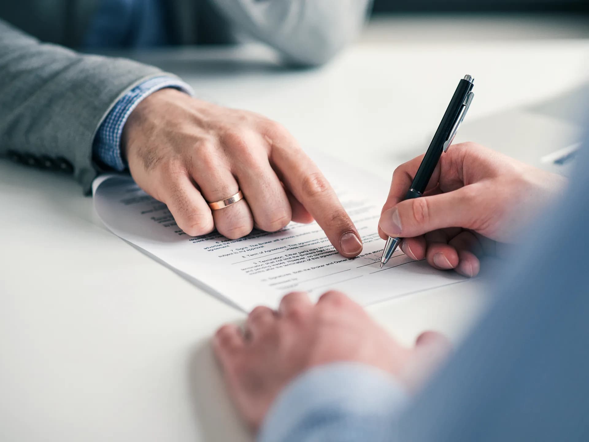 A hand pointing to a line of a document while another signs it